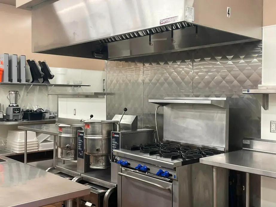 A commercial kitchen with kettles, a six-burner range and a long stainless hood