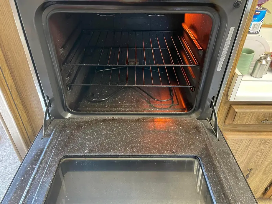 The inside of an open residential oven, racks and walls visible