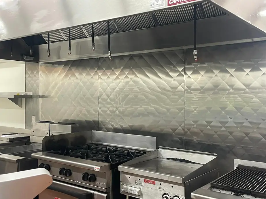 A commercial kitchen line with a stainless backsplash under the exhaust hood
