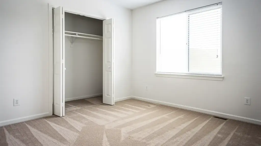 An empty bedroom with fresh vacuum lines in the carpet and an open closet wiped clean